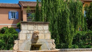 Une fontaine en pierre ornée d’une sculpture représentant la tête d’un lion, située dans une cour.