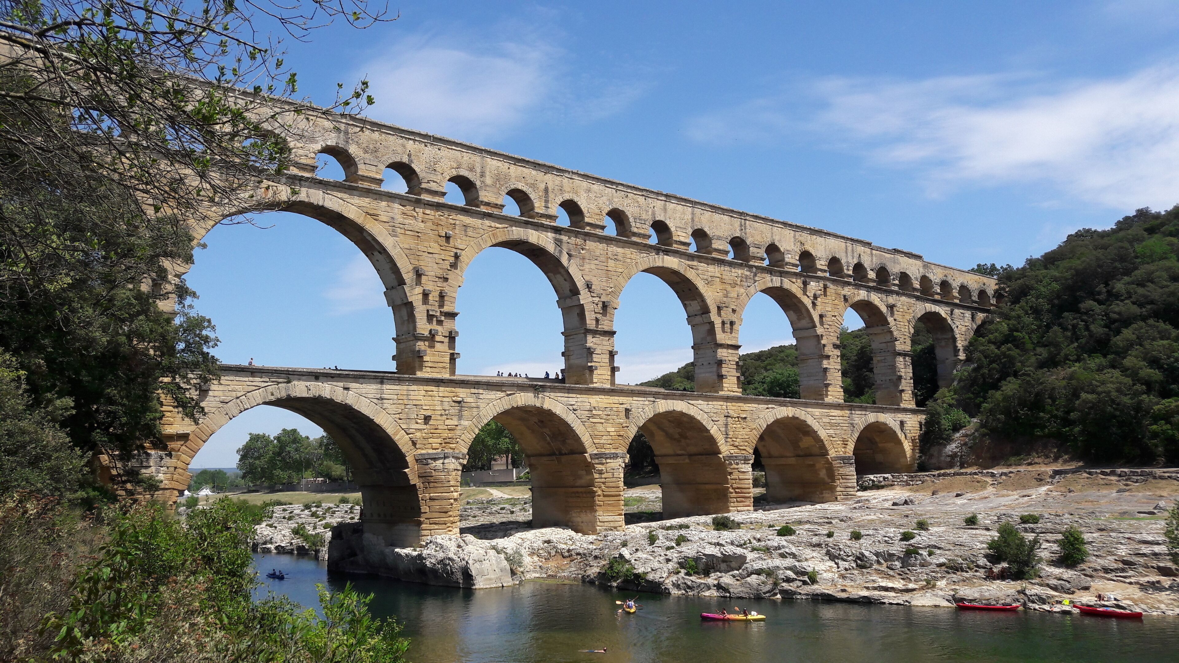 Un aqueduc en pierre, doté de plusieurs arches, enjambe une rivière et est entouré d’un paysage rocheux et de verdure.