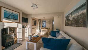 A cozy living room with a fireplace, a dining area, and a kitchen in the background. - Charming 2 bedroom cottage in Lymington, very close to town, marina & sea walks (Lymington)