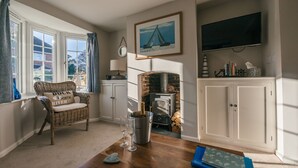 A cozy living room with a fireplace, a wicker chair, a table with a bottle of champagne, and a bookshelf. - Charming 2 bedroom cottage in Lymington, very close to town, marina & sea walks (Lymington)