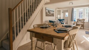 A dining area with a wooden table set for four, a staircase, and a view of the outdoors through a window. - Charming 2 bedroom cottage in Lymington, very close to town, marina & sea walks (Lymington)