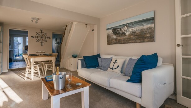 A living room with a white sofa, a wooden coffee table, and a painting of a boat on the wall. - Charming 2 bedroom cottage in Lymington, very close to town, marina & sea walks (Lymington)