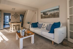 A living room with a white sofa, a wooden coffee table, and a painting of a boat on the wall.