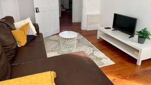 A living room with a brown sofa, a white coffee table, a flat-screen TV on a white stand, and a potted plant. - Kings' Retreat   (Horta)