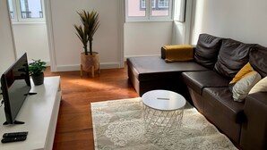 A modern living room with a brown leather sofa, a white side table, a small round table, a potted plant, and a flat-screen TV. - Kings' Retreat   (Horta)