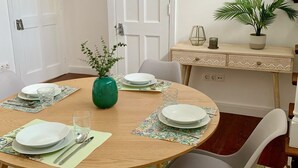 A dining area with a round table set for four, surrounded by chairs, a potted plant, and a staircase in the background. - Kings' Retreat   (Horta)
