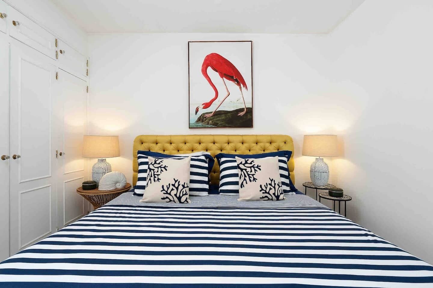 Ein Bett mit gestreifter Bettdecke, einem gelben, gepolsterten Kopfteil und zwei Nachttischlampen.