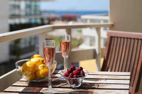 Un balcón con una mesa lista para dos personas, que incluye una copa de vino rosado, un cuenco de limones y un cuenco de cerezas.