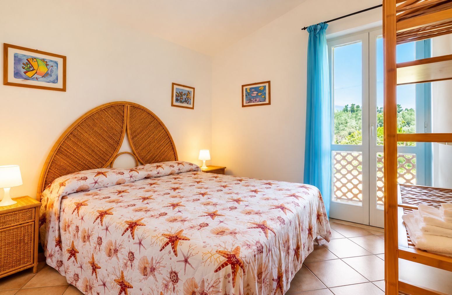 A bedroom with a bed, a nightstand, a lamp, a window with a view, and a wooden shelf with towels.
