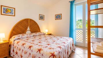 A bedroom with a bed, a nightstand, a lamp, a window with a view, and a wooden shelf with towels.