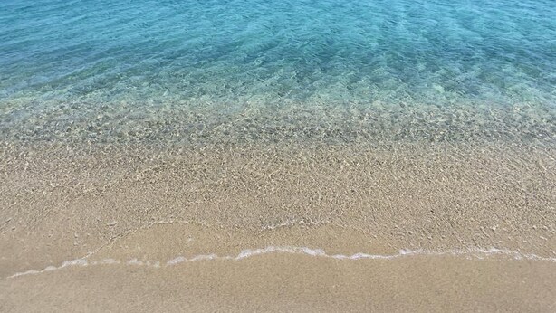Ein Strand mit klarem, flachem Wasser und sandigem Ufer.