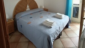Ein Schlafzimmer mit einem Bett, einem Nachttisch, einer Wandlampe und einem Fenster mit Vorhängen.