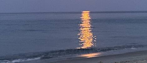 Escena de playa con un mar tranquilo y un reflejo visible de la luna en el agua.