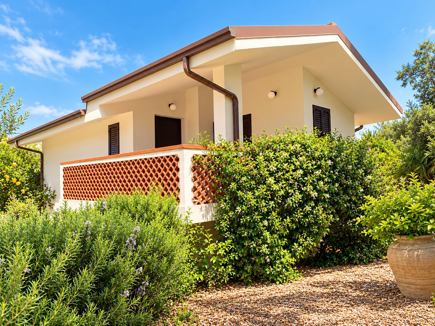 A modern two-story house with a balcony, surrounded by lush greenery and a clear sky.