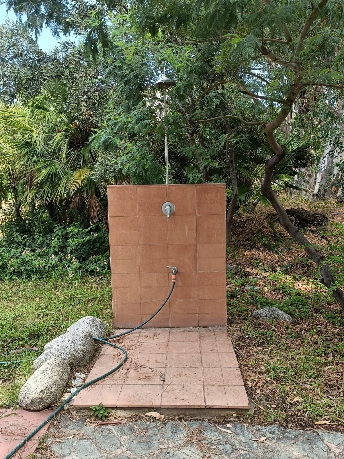 A small, enclosed outdoor shower area with a tiled floor and a hose connected to a faucet.