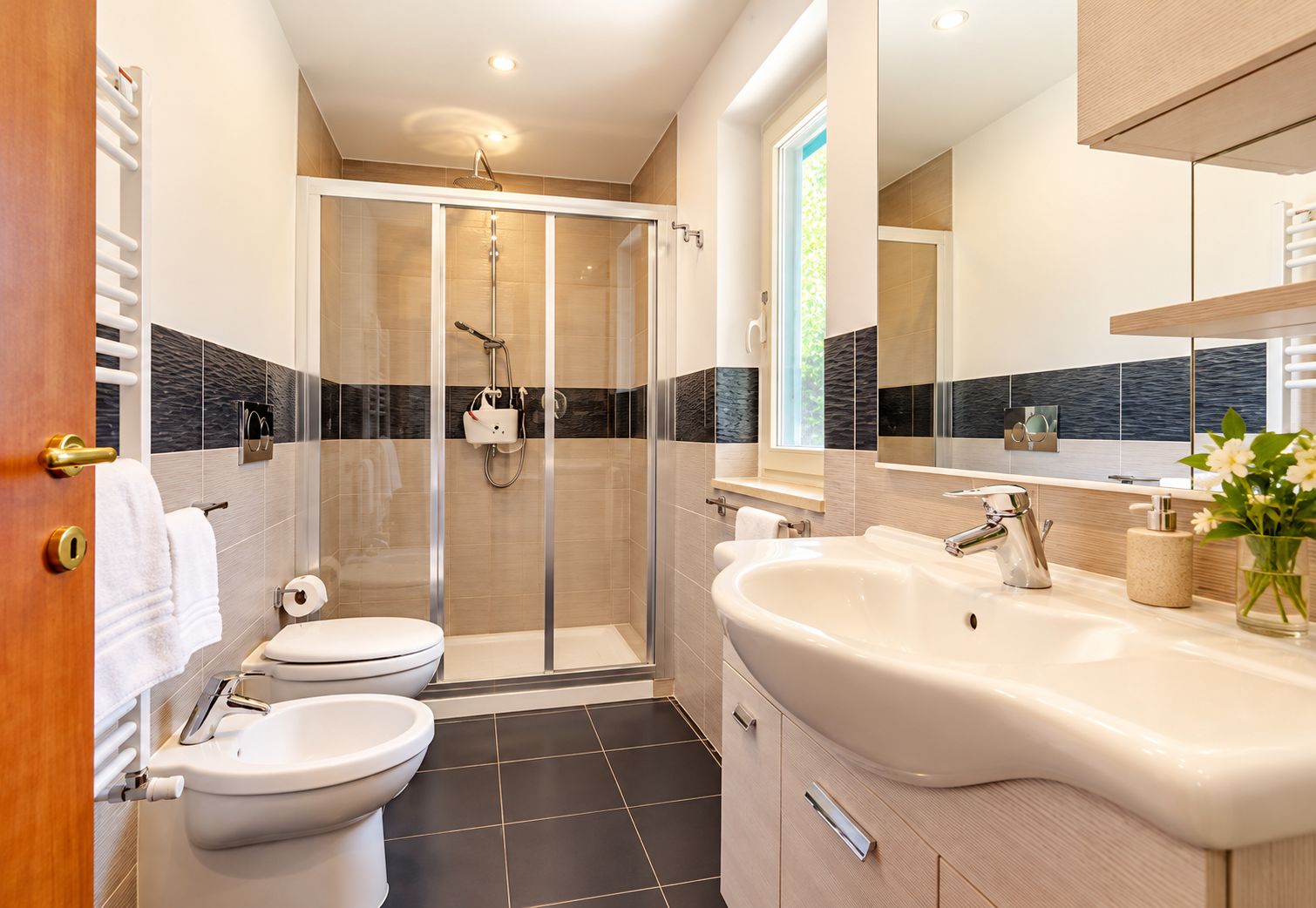A modern bathroom with a glass-enclosed shower, two toilets, a large sink, and a mirror above the sink.