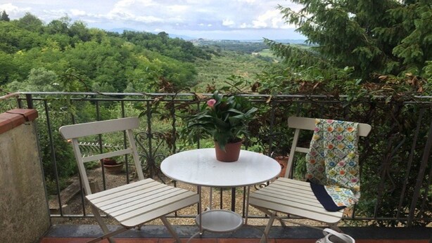 Een balkon met twee witte stoelen en een kleine tafel, omgeven door groen en een prachtig uitzicht.