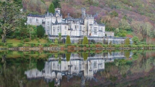 Un vaste château historique, doté de nombreuses tours et entouré de douves, au milieu d’une végétation luxuriante et bordé d’un lac paisible.
