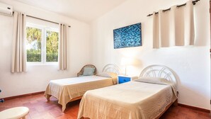Une chambre avec deux lits simples, une petite table et une fenêtre avec des rideaux.