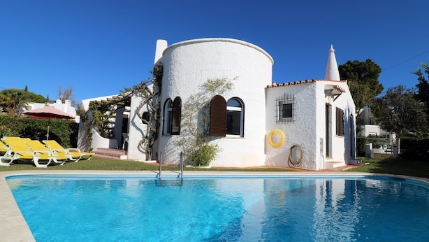 Un bâtiment blanc avec une piscine, des chaises longues jaunes et un ciel d’un bleu éclatant.
