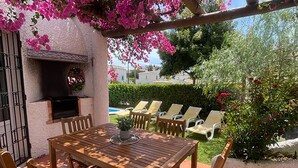 Une terrasse avec une table et des chaises en bois, entourée d’arbres à fleurs roses.