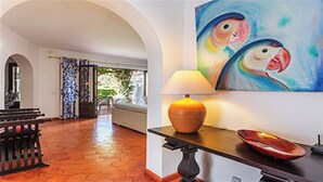 Une pièce avec un sol carrelé, un canapé, une table avec une lampe et un tableau représentant des oiseaux.