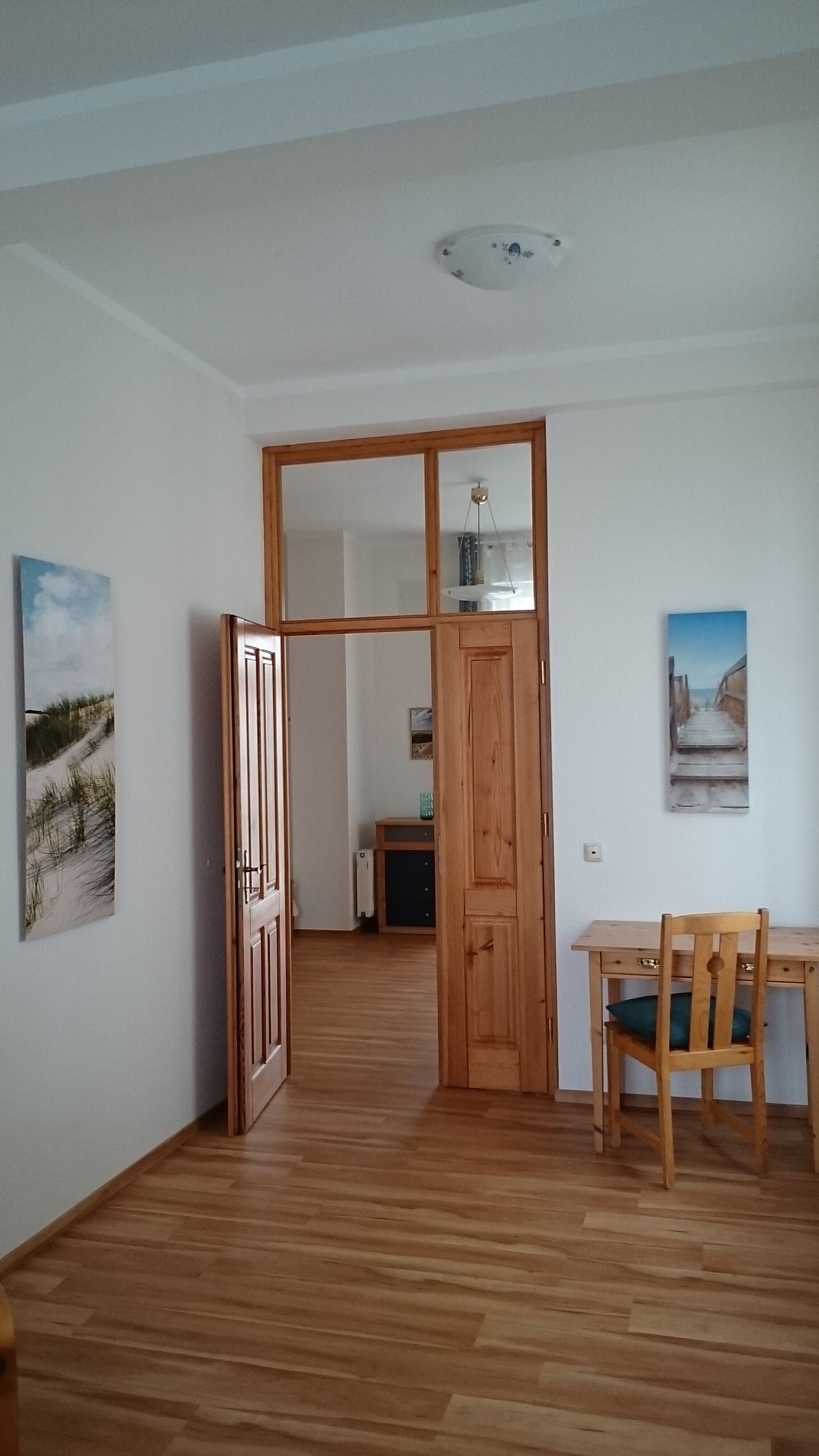 Una habitación con puerta de madera, una mesa de comedor con una silla y dos cuadros colgados en la pared.