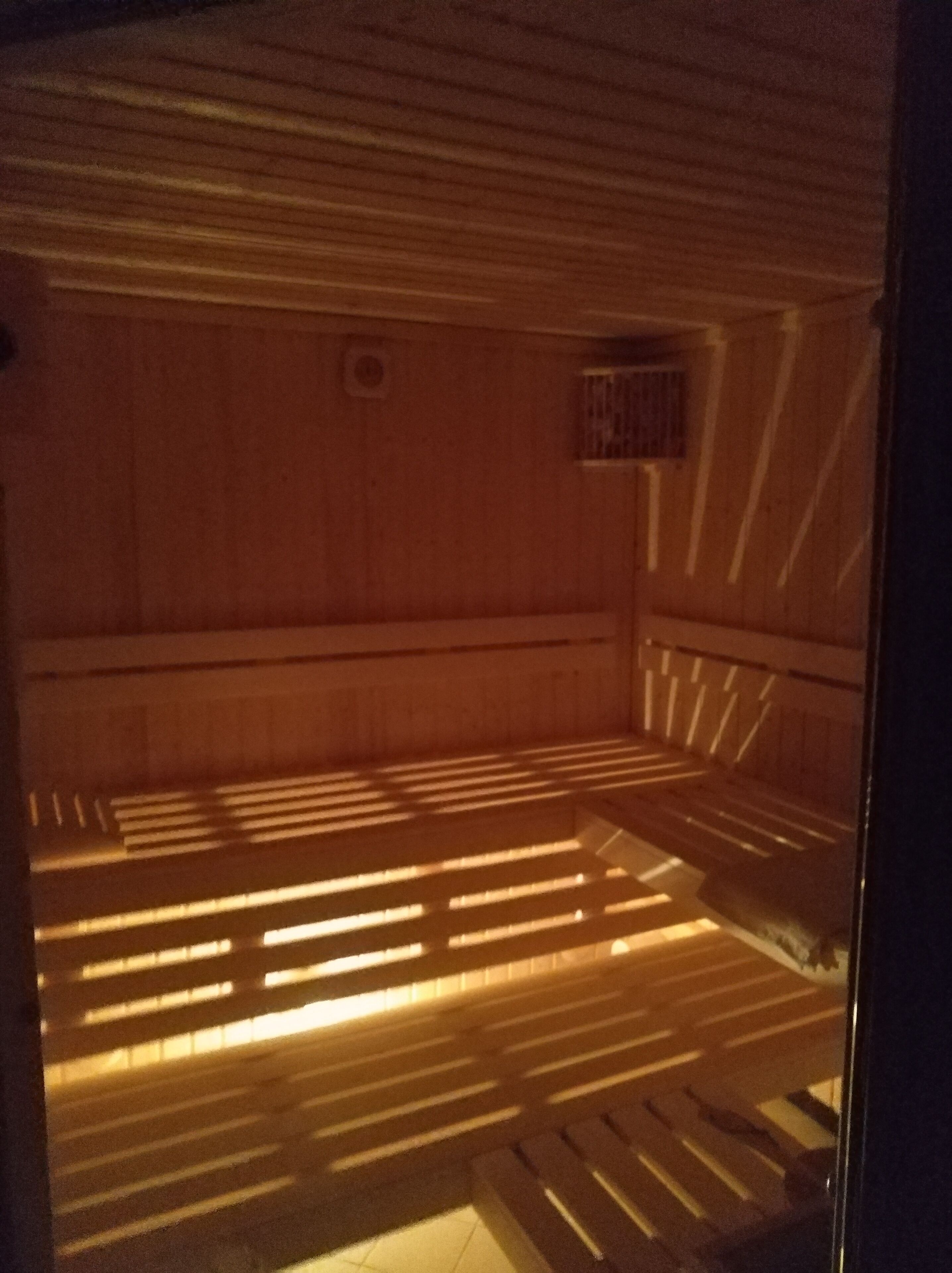 Eine Sauna mit in Reihen angeordneten Bänken, einem kleinen Fenster und einer Tür.