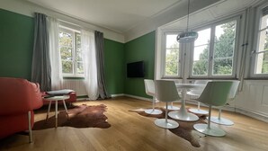 A room with a green wall, a wooden floor, a red sofa, a white table with four chairs, and a television on the wall. - 3 bedroom Jugendstilwohnung near the castle (Ludwigsburg)