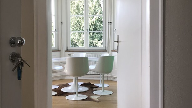 A room with a wooden floor, white walls, and a large window with a view of trees. There are two white chairs and a white table in the room. - 3 bedroom Jugendstilwohnung near the castle (Ludwigsburg)