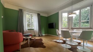 A modern living room with a red sofa, a dining table with chairs, a television mounted on the wall, and large windows with curtains. - 3 bedroom Jugendstilwohnung near the castle (Ludwigsburg)
