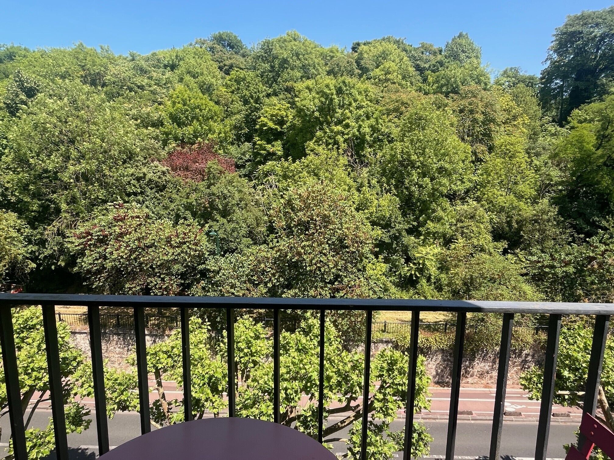 Een balkon met uitzicht op een dicht bos en een weg in de verte.