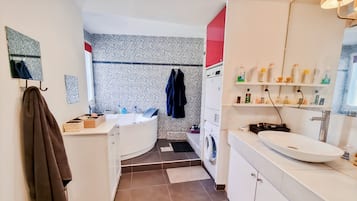Une salle de bain moderne avec une baignoire sur pieds, un lave-linge encastré et un grand meuble-lavabo.