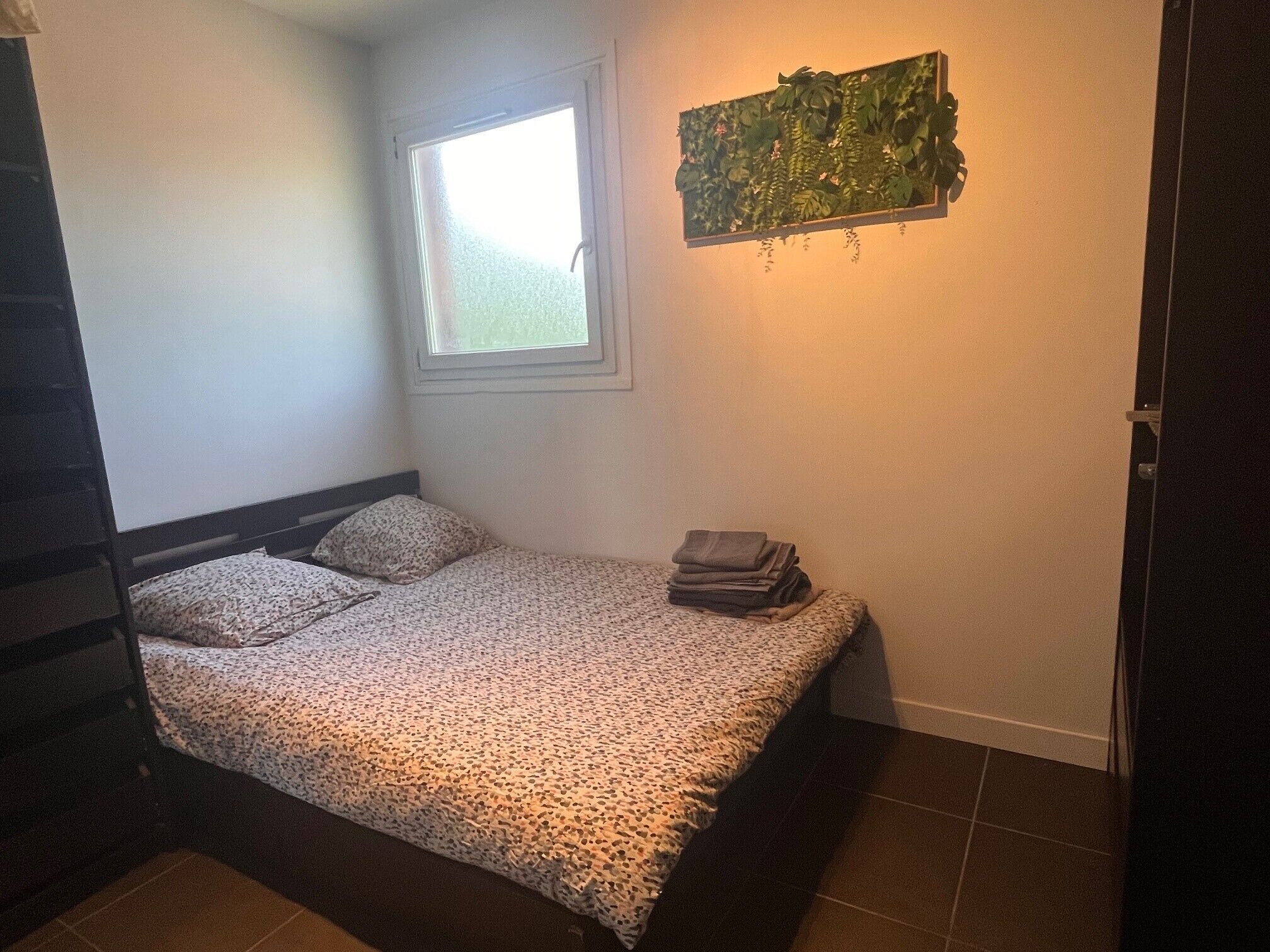 A bedroom with a bed, a window, and a wall-mounted plant.