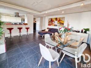 A modern living room with a glass dining table, white chairs, a sofa, and a red bar stool. - Appt Cosy Porte Paris Bercy / Parc Floral de Vincennes + Parking (Saint maurice)