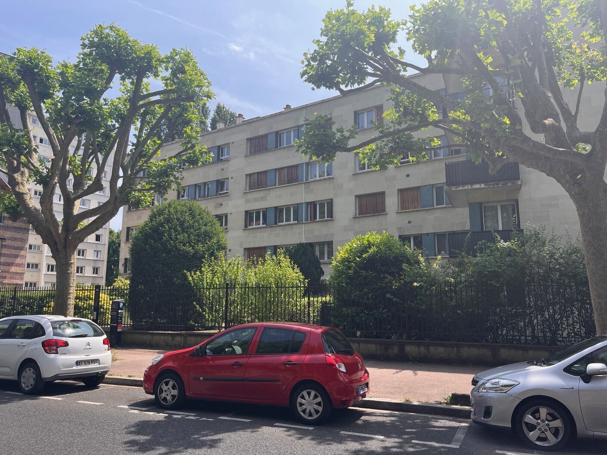 Un edificio residencial de varios pisos con fachada plana, amplias ventanas y una entrada protegida por una reja.