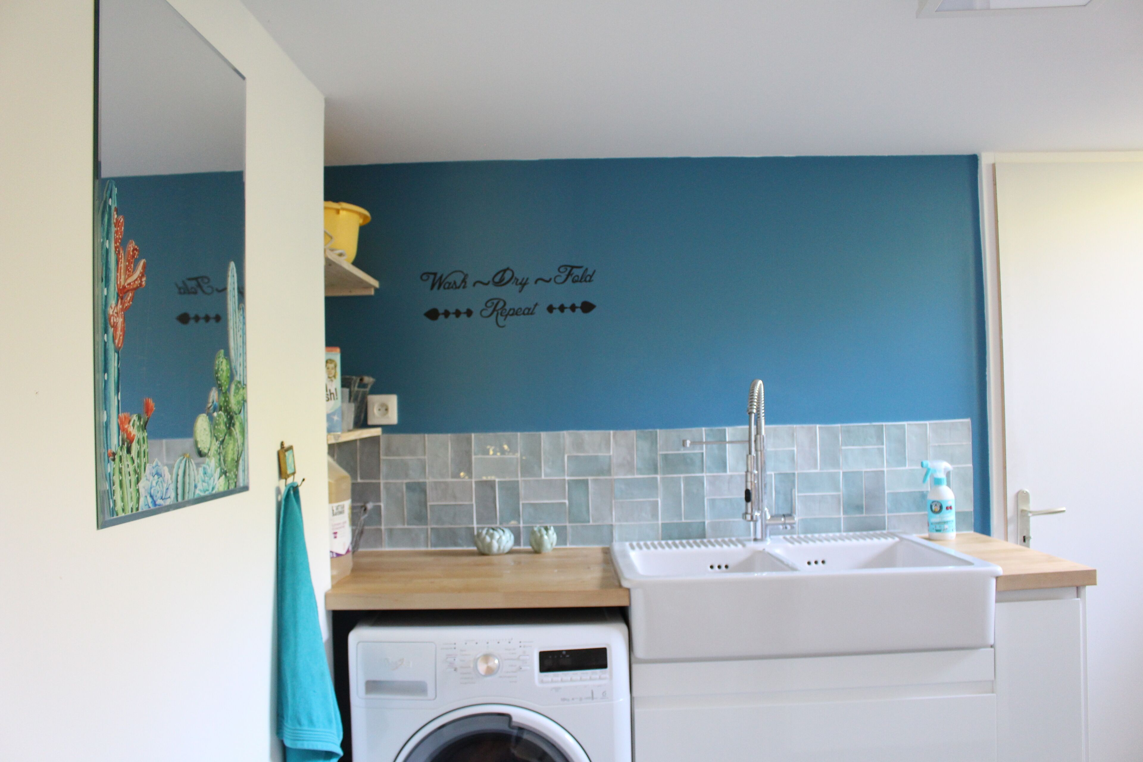 Uma cozinha com máquina de lavar, pia e parede azul com a inscrição 'Wash, Dry, Fold'.