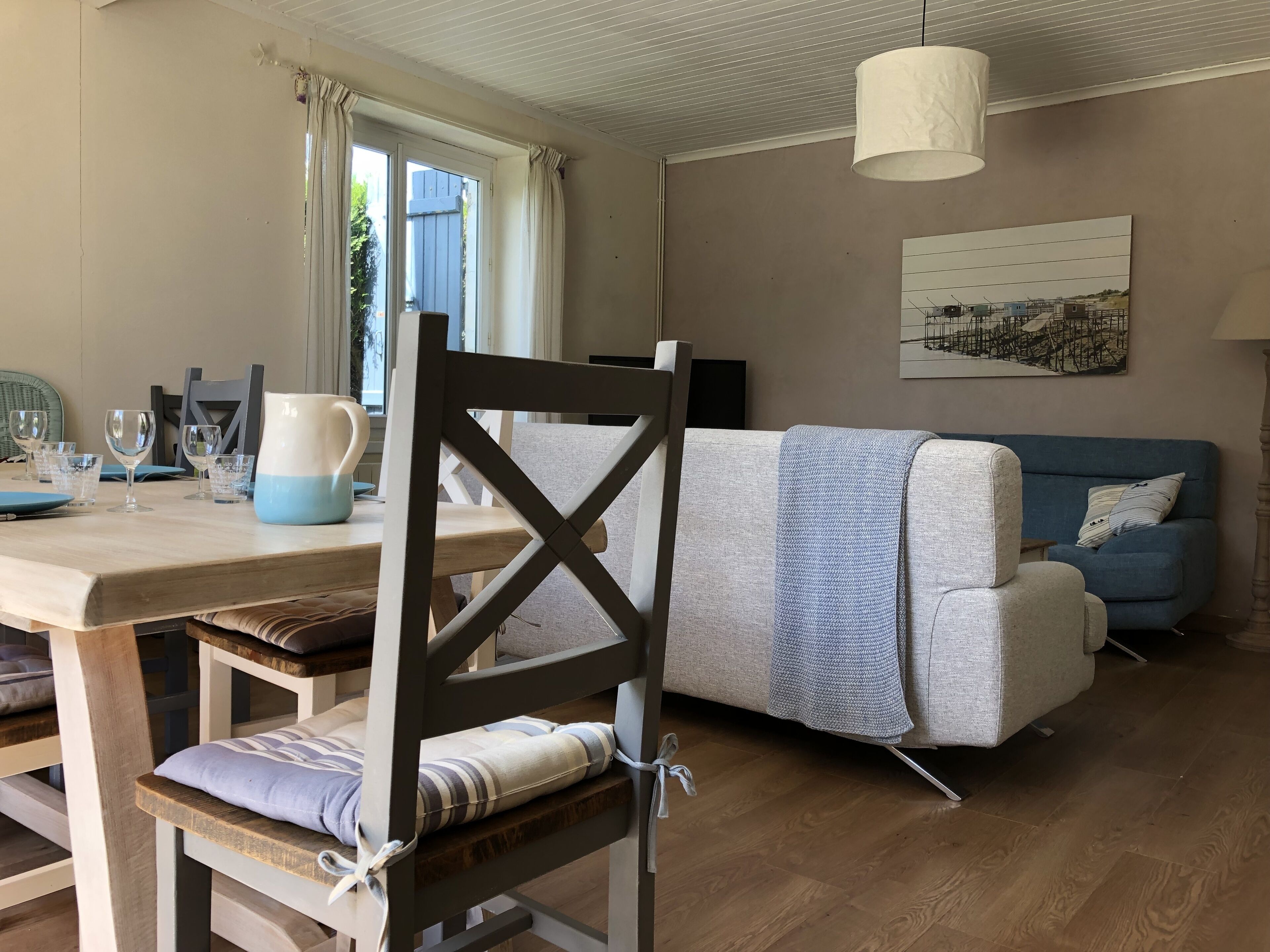 Un salón acogedor con una mesa de comedor preparada para cuatro personas, un sofá y una silla con cojín.