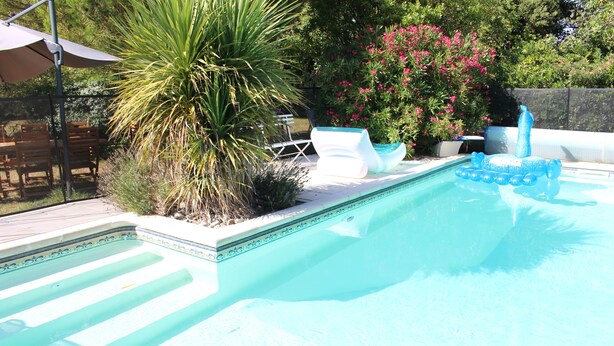 Una piscina con una característica de agua azul cristalina, rodeada de un patio con sillas y una mesa.