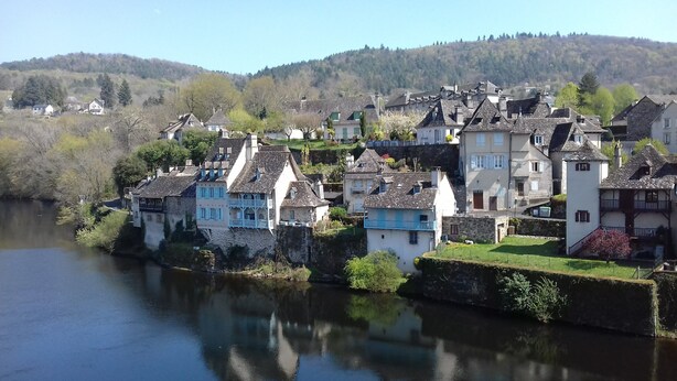 A riverside town with historic buildings, a stone bridge, and a hill in the background.