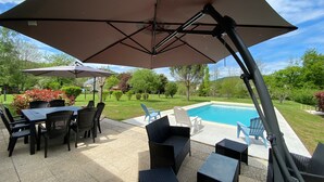 An outdoor patio area with a pool, outdoor furniture, and umbrellas.