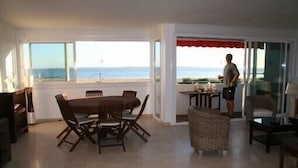 A spacious living area with a large dining table and chairs, a wicker sofa, and a view of the beach through large windows. - Apart. w/ panoramic sea view facing beach for 6 people, Saint-Georges-de-Didonne (Saint-Georges-De-Didonne)