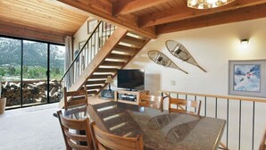 A spacious dining area with a large table and chairs, a wooden staircase, and a television on a stand. - Snowflower 15: Mountain Views, Near Snowcreek Golf (Mammoth Lakes)