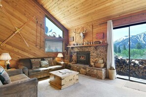Interno accogliente di una baita con camino in pietra, mobili in legno e vista sulle montagne.
