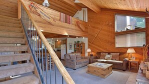 A wooden interior with a staircase, a living room with sofas, a fireplace, and ski equipment. - Snowflower 15: Mountain Views, Near Snowcreek Golf (Mammoth Lakes)