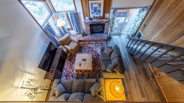 A spacious loft-style living area with a fireplace, a wooden staircase, and a view of the outdoors. - Sunrise15: close to Snowcreek Golf Course (Mammoth Lakes)