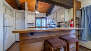 A kitchen with wooden beams, white cabinets, a wooden island with stools, a window, and a fire extinguisher. - Sunrise15: close to Snowcreek Golf Course (Mammoth Lakes)