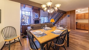A dining area with a wooden table set for four, a chandelier, and a staircase leading to a kitchen. - Sunrise15: close to Snowcreek Golf Course (Mammoth Lakes)