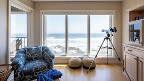 A room with a large window overlooking the beach, a tripod with a camera, and a patterned armchair. - Sur La Plage-Oceanfront & Pool (Fernandina Beach)