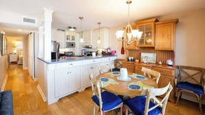 A modern kitchen with white cabinets, a central island, and a dining area with blue chairs. - Sur La Plage-Oceanfront & Pool (Fernandina Beach)